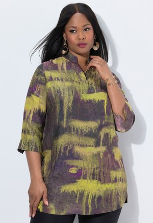 Multicolored tunic featuring a purple and green abstract pattern, a standing collar, and three-quarter sleeves. Worn over black pants.