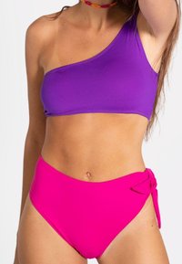 Top de bikini morado de un solo hombro combinado con braguitas de bikini rosas de cintura alta que cuentan con un lazo de acento en el costado. Textura de tela suave.