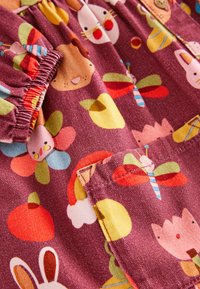Child's clothing fabric in maroon featuring animal and flower patterns. Soft texture with pleated detailing and pocket on the front.