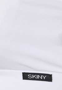 Tecido de algodão branco com uma textura suave. Uma etiqueta preta com o nome da marca "SKINY" é visível ao longo da borda.
