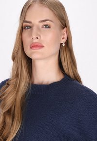 Pulover tricotat bleumarin cu guler rotund. Modelul are părul lung și ondulat și poartă cercei cu perle. Textură netedă, design simplu.