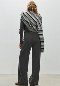 Top lavorato a maglia grigia a maniche lunghe abbinato a pantaloni grigi a gamba larga; sciarpa con accenti a righe grigio chiaro e blu navy drappeggiata sulle spalle.