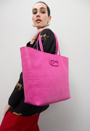 Bolso tote rosa hecho de material texturizado, con letras en relieve y un adorno circular de metal. Asa doble resistente para llevar.