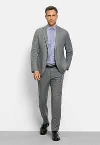 Grau maßgeschneiderter Anzug mit einem dezenten Muster, kombiniert mit einem hellblauen und weißen gestreiften Hemd sowie schwarzen Schnürschuhen.