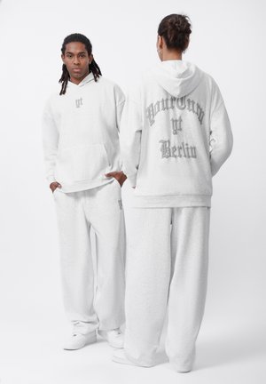 Haut de survêtement en coton gris clair et pantalon de survêtement assorti, avec une poche avant et un grand design textuel au dos en gris plus foncé.