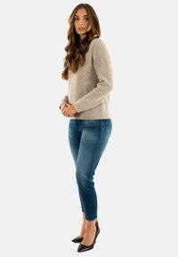 Maglione a coste di un beige chiaro con maniche lunghe, abbinato a jeans blu attillati e scarpe nere a punta, creando un outfit casual.