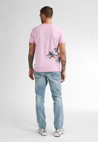 Camiseta rosa de manga corta con gráfico de palmera en la parte posterior, combinada con jeans de color azul claro y zapatillas blancas. Material de algodón suave.
