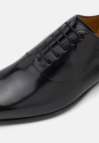 Fekete bőr elegáns cipő, fényes felülettel, kerek orral és hat pár fűzőlyukkal, karcsú sziluettel és diszkrét varrásokkal.