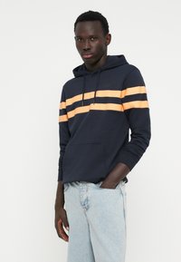 Navy hoodie with orange horizontal stripes, featuring a front pocket and drawstring hood. Fabric has a soft texture, designed for comfort.