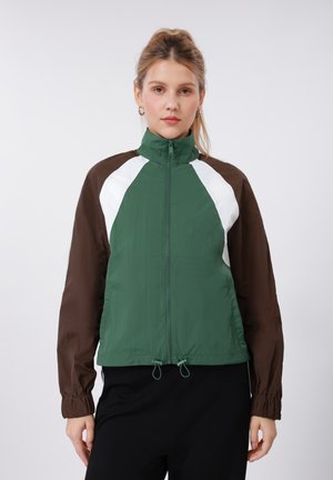 Πράσινο, καφέ και λευκό μπουφάν αδιάβροχο με ψηλό γιακά, ελαστικά μανίκια και ρυθμιζόμενο τελείωμα. Ελαφρύ, με λεία υφή, αθλητικός σχεδιασμός.