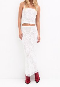 Conjunto de top corto de encaje blanco y falda maxi, con un diseño ajustado, patrones florales texturizados y tirantes finos. Combinado con botas rojas de punta.