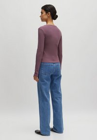 Langes lila Oberteil mit figurbetontem Design, kombiniert mit hellblauen weiten Jeans. Glatte Textur, minimalistischer Stil und klassische Taschen.