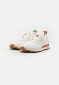 Bílé pletené tenisky s texturovaným svrškem, které mají barevné akcenty v růžové, tyrkysové a oranžové barvě, a světlou hnědou gumovou podrážku.