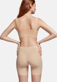 Nude seamless bra and shorts set made of smooth, stretchy fabric. The shorts have a mid-thigh length and a scalloped waistband for comfort.