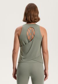 Sleeveless athletic top in light green fabric, featuring a layered back design with crisscross straps and a fluid drape. Minimal branding visible.