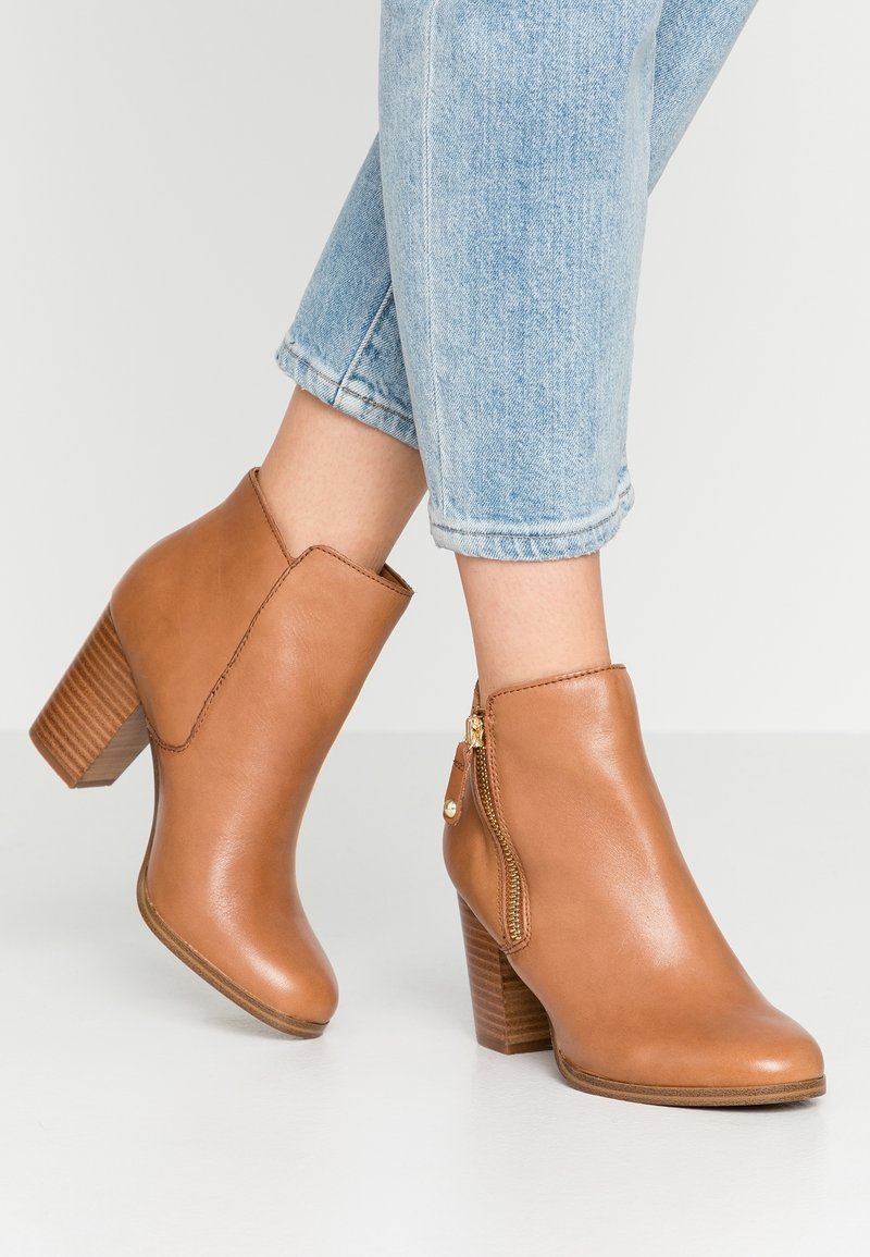 Jean en denim bleu clair retroussé à la cheville, porté avec des bottines en cuir marron clair dotées de talons épais superposés et de fermetures éclair latérales.