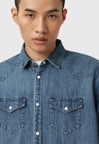 Denimskjorta i medelblått, med tryckknappar, westernstil med yoke och två bröstfickor med spetsiga lock. Strukturerad tyg.