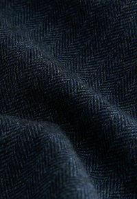 Marineblaue Stoff mit Fischgrätenmuster, der sich weich und strukturiert anfühlt, mit komplexen diagonalen Linien und einem subtilen Glanz.