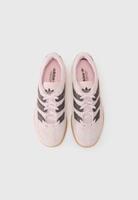 Ανοιχτό ροζ σουέτ αθλητικά παπούτσια με μαύρες ρίγες, στρογγυλή μύτη και υφασμάτινη σόλα από καουτσούκ. Διαθέτει λογότυπο στην γλώσσα και στο εσωτερικό.