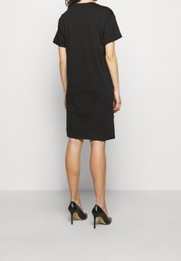 Robe t-shirt noire à coupe décontractée, avec des manches courtes retournées, un ourlet droit et une texture de coton lisse ; assortie à des escarpins noirs.