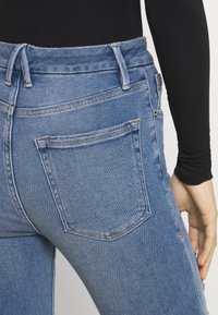 Jeans de denim azul claro con cintura alta, costuras visibles y un bolsillo trasero. El material parece ligeramente desgastado cerca del dobladillo.