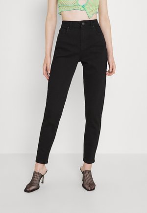 Zwarte high-waisted jeans met een getailleerd silhouet, vijf zakken en een knoopsluiting, gecombineerd met zwarte geperforeerde hakmuilen.