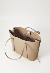 Beige totebag lavet af glat materiale, med to lange håndtag, en lynlåslukning og en indvendig lomme med et label.