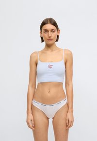 Ανοιχτό μπλε αδιάκοπο σουτιέν με λεπτές τιράντες, με μικρό κόκκινο λογότυπο "Calvin Klein". Λευκά εσώρουχα με μαύρη ταινία λογότυπου.