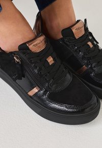Black sneakers with a mix of shiny patent leather and soft suede. Features bronze accents, a side zipper, and textured surfaces.