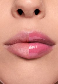 Producto de labios mostrado sobre los labios, un lado rosa claro mate, el otro lado rosa brillante brillante, textura suave, fondo de tono de piel natural.