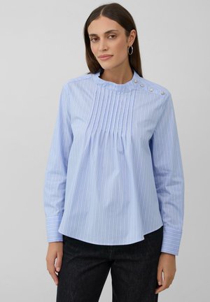 Blusa azzurra a maniche lunghe con strisce bianche verticali, pieghe sul davanti e bottoni decorativi lungo il colletto. Tessuto dalla consistenza liscia.