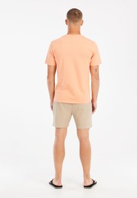 Lichtoranje katoenen t-shirt, korte mouwen, ronde hals, gecombineerd met beige shorts, met textuur, boven de knie, en zwarte flip-flops.