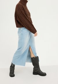 Hnědý pletený rolák, světle modrá džínová sukně s bočním rozparkem a černé kožené vysoké boty s přezkami a cvočky.