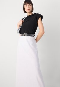 Black fitted top with short cap sleeves, paired with a flowy white skirt. Accessorized with a black studded belt and clear handbag.