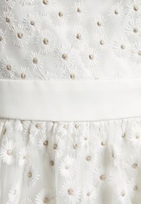 Abito bianco con ricami floreali, caratterizzato da margherite testurizzate e dettagli in filo metallico, con una vita liscia e sovrapposizione in tulle.