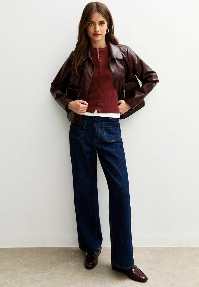 Burgundy leather cropped jacket, ribbed burgundy cardigan, white shirt, dark blue wide-leg jeans, and dark burgundy shoes. Simple design and textures.