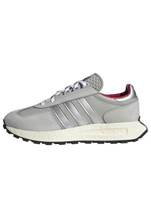 Szary sneaker Adidas z białymi sznurowadłami, trzema srebrnymi paskami po bokach, białą fakturowaną środkową podeszwą i czarną podeszwą zewnętrzną.