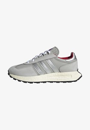 Szary sneaker Adidas z białymi sznurowadłami, trzema srebrnymi paskami po bokach, białą fakturowaną środkową podeszwą i czarną podeszwą zewnętrzną.