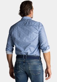 Lichtblauw gestreept shirt met opgerolde mouwen, voorzien van kleine gekleurde stippen. Draagt met blauwe denim jeans en een geweven riem.