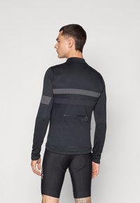 Black long-sleeve cycling jersey with gray reflective stripes, zippered pocket, and smooth texture. Worn with black padded cycling shorts.