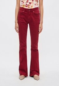 Punaiset liehuhousut, valmistettu denimmateriaalista; niissä on viisi taskua, vyölenkit ja metalliset napit; sileä pinta; yhdistetty koristeltuihin, kärjestä teräväkärkisiin kenkiin.