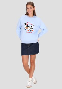 Világoskék pulóver fekete-fehér kutyás grafikával, piros felirattal és bordázott derékrésszel. Farmer szoknyával és fehér sportcipővel párosítva.