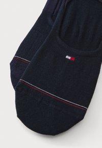 Temno modre gležnjarice iz strukturirane pletenine, ki imajo bel in rdeč poudarek v obliki črt in majhno logotip v rdeči, beli in modri barvi.