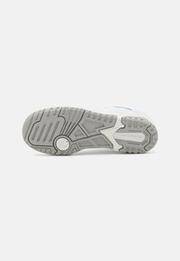 Weiße und hellgraue Sneaker-Sohle mit einem strukturierten Gummidesign, ausgeprägten Profilmustern und einem kreisförmigen Logo in einem Farbverlauf.