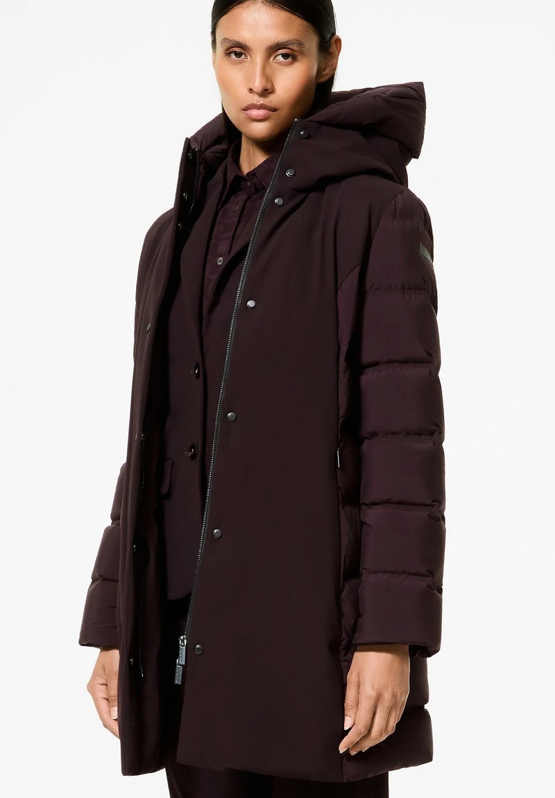 Piumino bordeaux con cappuccio, dotato di chiusura con zip e bottoni a pressione, tasche laterali e maniche trapuntate testurizzate. Design leggero e caldo.