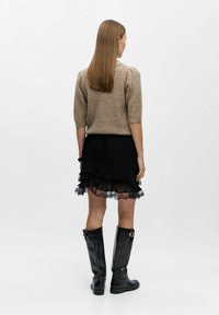 Beżowy sweter dzianinowy z krótkimi rękawami, warstwowa czarna spódnica plisowana z koronkowym wykończeniem oraz czarne skórzane buty do kolan z detalem z klamrą.