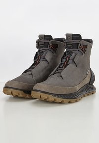 Bottes de randonnée grises au design robuste, avec des matériaux en daim texturé et maille, des accents orange et une semelle en caoutchouc rugueuse pour une bonne traction.