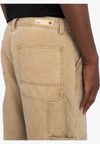 Beige cargo bukser lavet af en blanding af bomuldsstof. Har stor baglomme, flad talje og diskrete syninger.