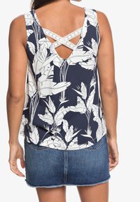 Granatowy top bez rękawów z białym nadrukiem kwiatowym, z tyłu w kształcie litery V z krzyżującym się detalem z koronki. Połączony z dżinsową spódnicą mini.