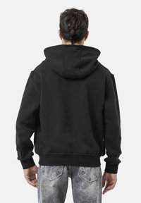 Schwarzer Kapuzenpullover aus Baumwollmischung, mit lockerer Passform, gerippten Bündchen und Saum. Sichtbare Nähte und ein einzelnes Kängurutaschen-Detail.